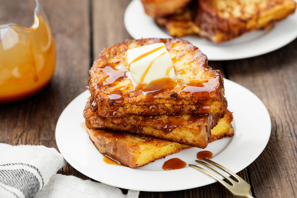 plate of French Toast sitting on a table with some syrup in a small pitcher